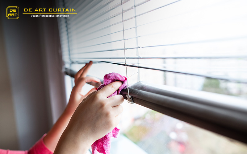Hand of young woman cleaning blinds by pink cloth